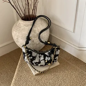 Chic hobo bag with black and white cow print, long strap, and gold metal chain link details