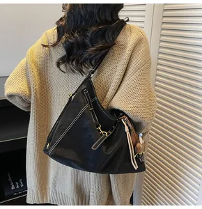 Detail of black tote bag with white contrast stitching and gold tassels on model