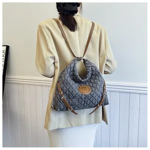 Detail of grey quilted backpack with brown leather straps and M logo on a model