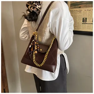 Brown suede tote bag with gold chain strap and wooden bead charm on a white top