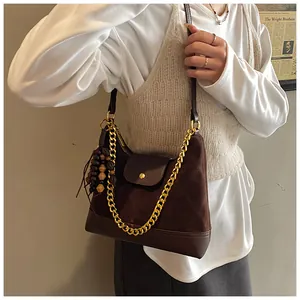 Detail of dark brown suede shoulder bag with thick gold chain and wood bead charm