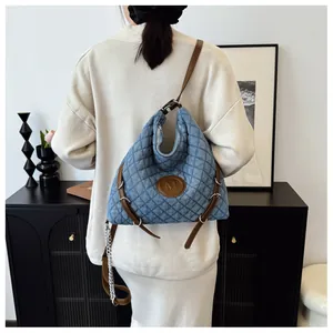 Detail of blue quilted denim tote bag with brown leather strap and silver chain accent