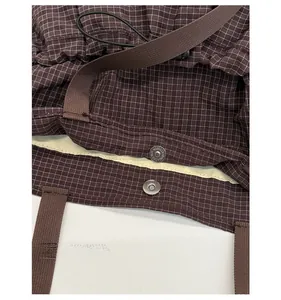 Detail shot of the magnetic snap closure on a brown checkered tote bag with woven strap