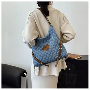 Detail of blue quilted denim tote bag with leather logo patch and metal chain strap