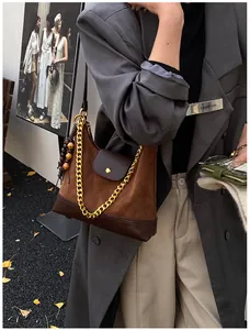 Detailed shot of brown suede tote bag featuring gold chain strap and wooden bead tassel