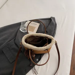 Brown suede tote bag with cream fleece trim and decorative pom-poms on grey suit