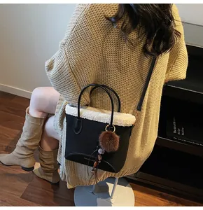 Detail of black suede bucket bag with white faux fur trim and pompom charm on a model