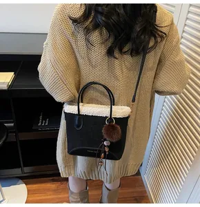 Detail of black suede bucket bag with white faux fur trim and brown pom-pom charm