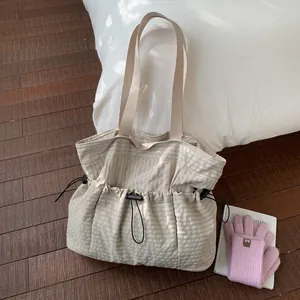 Detail of light beige plaid canvas tote bag with black drawstring closure on wood floor