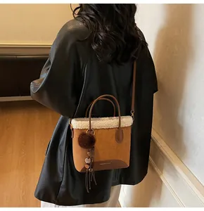 Detail of brown suede bucket bag featuring white faux shearling trim and plush pompom charm