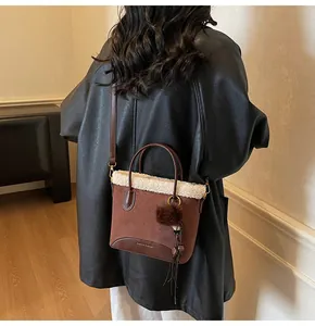 Detail view of suede bucket bag with shearling trim worn over a black leather jacket