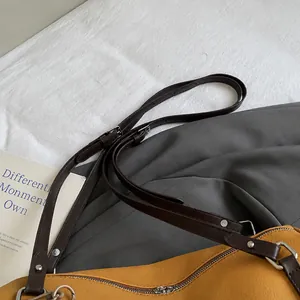 Detail des verstellbaren dunkelbraunen Leder-Schultergurts mit Silberschnalle an gelber Tasche