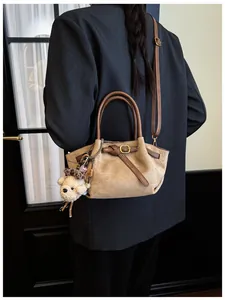 Detalle del bolso tote de ante caqui con hebillas de bronce y un colgante de osito