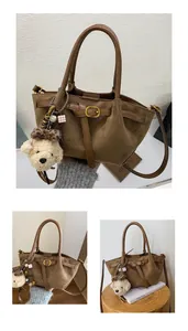 Detalle de bolso tote de ante marrón con colgante de osito de peluche y hebillas de metal