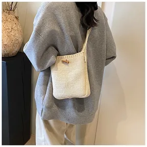 Detail of minimalist cream knit crossbody bag with wooden button closure on model
