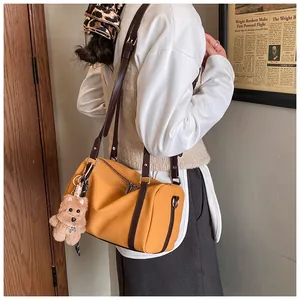 Gelbe Zylindertasche mit braunen Riemen und Plüschbär-Anhänger, getragen von einem Model