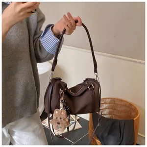 Detail der dunkelbraunen Zylindertasche mit Bärenanhänger und verstellbarem Schultergurt