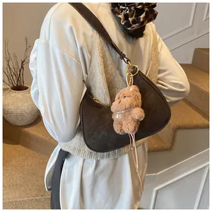 Detail view of brown suede crescent bag with a cute plush bear charm accessory
