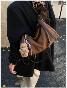 Detail einer dunkelbraunen Ledertasche mit Plüschbär-Anhänger und Leoparden-Halstuch
