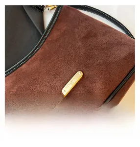 Close-up of brown suede fabric with gold logo plaque and black leather trim detail