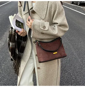 Detail of dark brown suede shoulder bag with gold metal plate and black leather handle