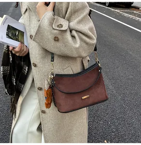 Close-up of deep brown suede shoulder bag with gold hardware and cute bear charm