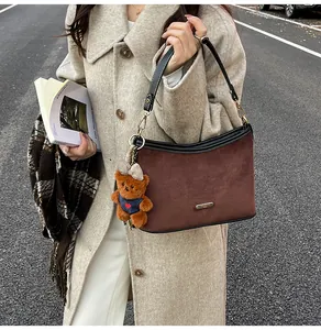 Detail of dark brown suede shoulder bag featuring metal logo and cute bear pendant charm