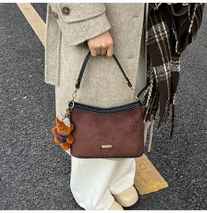 Detail of dark brown suede handbag featuring black leather trim and a cute plush bear charm