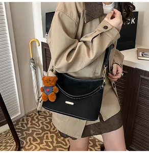 Detail of black crossbody bag with white stitching and cute brown bear charm
