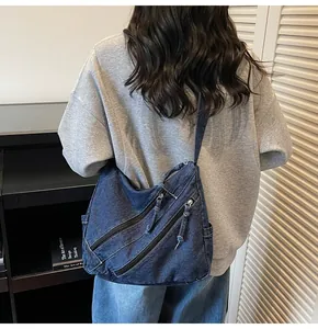 Detail shot of a dark blue denim hobo bag featuring tassel zippers and a casual style