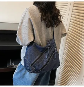 Detail of dark blue denim crossbody bag featuring multiple pockets and knotted zipper pulls