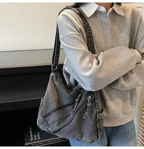 Detail of dark grey washed denim hobo bag featuring multiple diagonal zippers and wide strap