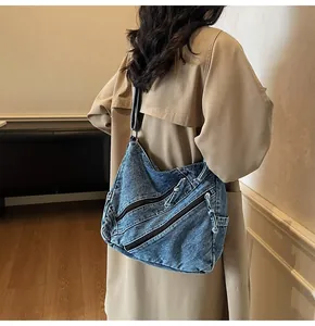 Detail of blue washed denim hobo bag featuring three black diagonal zipper pockets