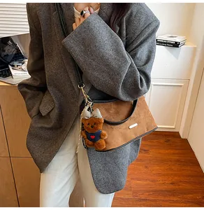 Brown suede crossbody bag with teddy bear charm and black leather trim on a grey blazer