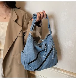 Detail of blue washed denim tote bag with side pockets and decorative zippers on model