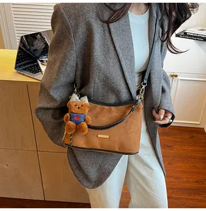 Brown suede crossbody bag with teddy bear charm shown on a model in a warm indoor setting