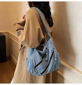 Detail of light blue washed denim shoulder bag featuring moto-style zipper pockets