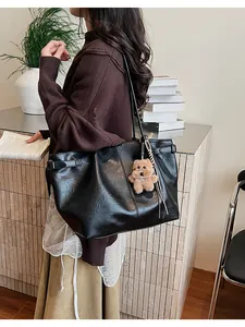 Detail of a black textured leather tote bag with a brown teddy bear charm on shoulder