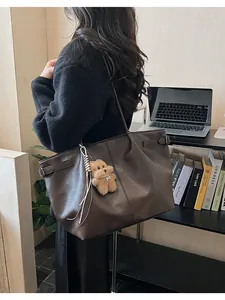 Detailed close-up of dark brown leather tote bag with a cute plush bear charm accessory