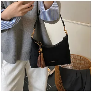 Detail of black suede hobo bag with brown tassel pendant and gold metal hardware