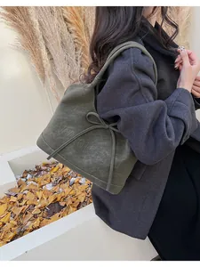 Detail of green suede tote bag with large bow and embossed logo in autumn setting
