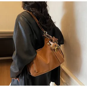 Détail latéral d'un grand sac à bandoulière en daim caramel avec fermetures métalliques