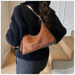 Detail of brown suede shoulder bag with leather tassel decoration and embossed logo
