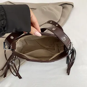 Sac bandoulière en similicuir marron foncé avec pompons et œillets argentés sur la sangle