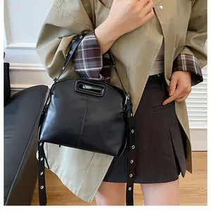 Détail du sac en cuir noir avec bandoulière à œillets et poignée découpée ovale