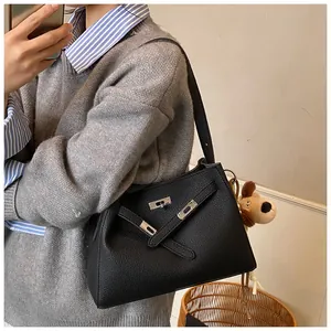 Detail of black lychee grain leather handbag featuring metal clasp and plush puppy charm