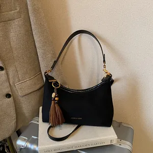 Retro black suede dumpling bag with leather trim and tassel charm on books