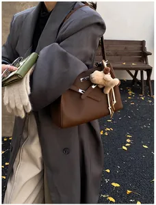 Close-up of brown pebbled leather bucket bag with metallic hardware and cute dog charm