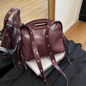 Sac à main en cuir bordeaux avec franges et œillets argentés vue dans un miroir