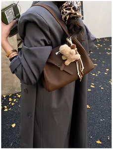 Detail of brown litchi pattern leather bucket bag with metal buckle and teddy bear charm